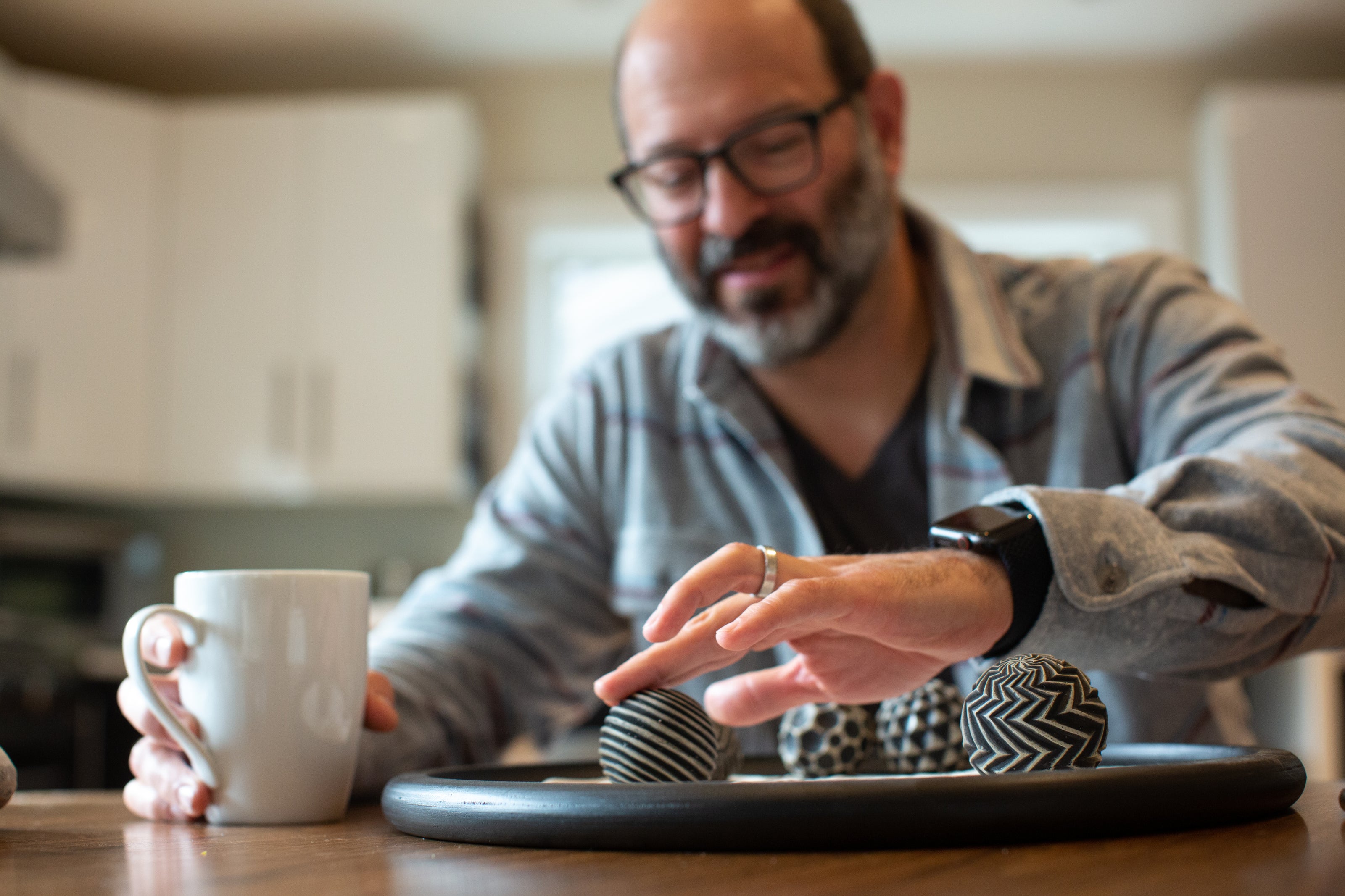 Man playfully rolling his sand scape sand orbs with the tips of his fingers while enjoying his morning coffee